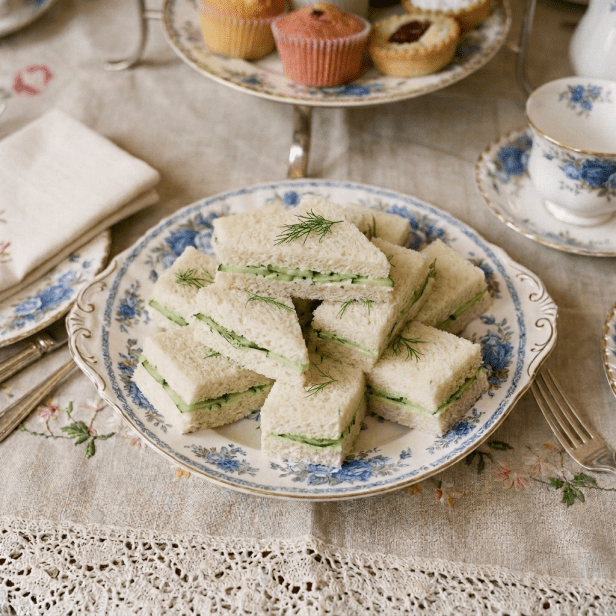 Small cucumber tea sandwiches garnished with dill on a decorative plate
